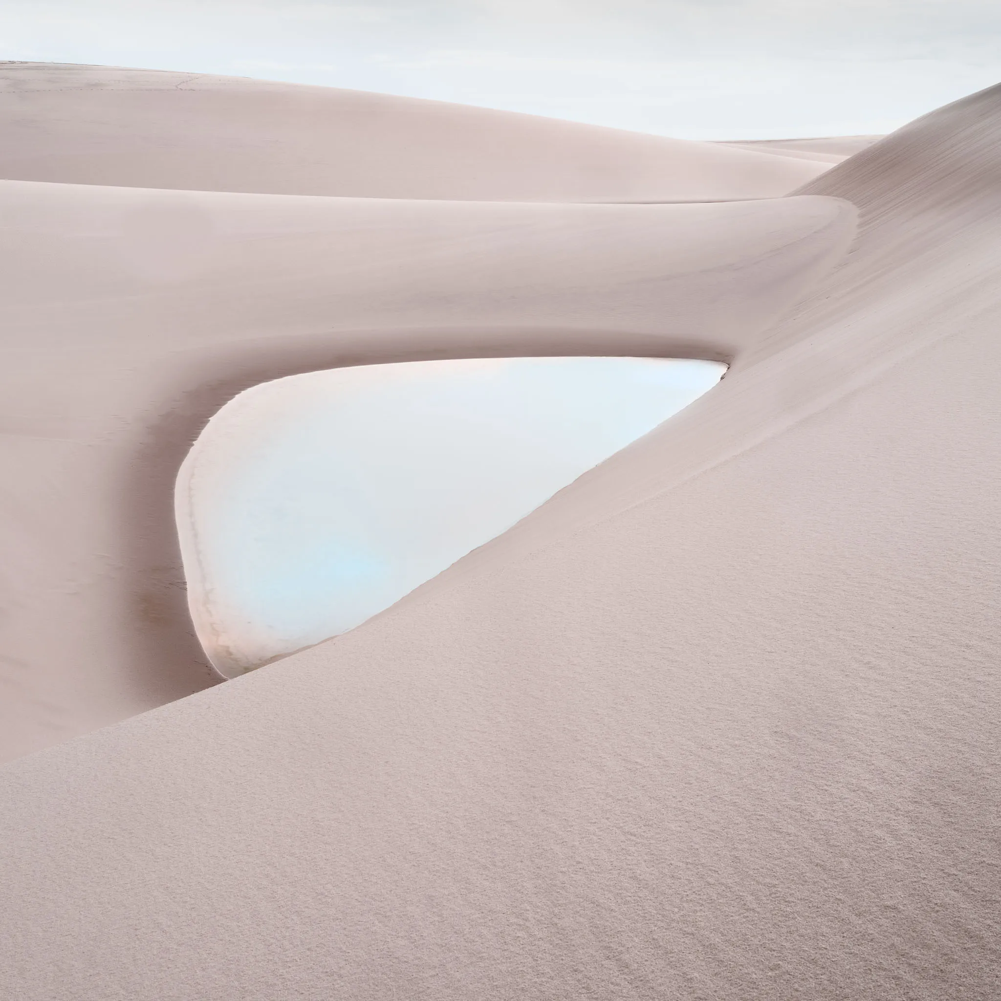 Smooth pale dunes curving around a small soft-white lagoon under a muted sky