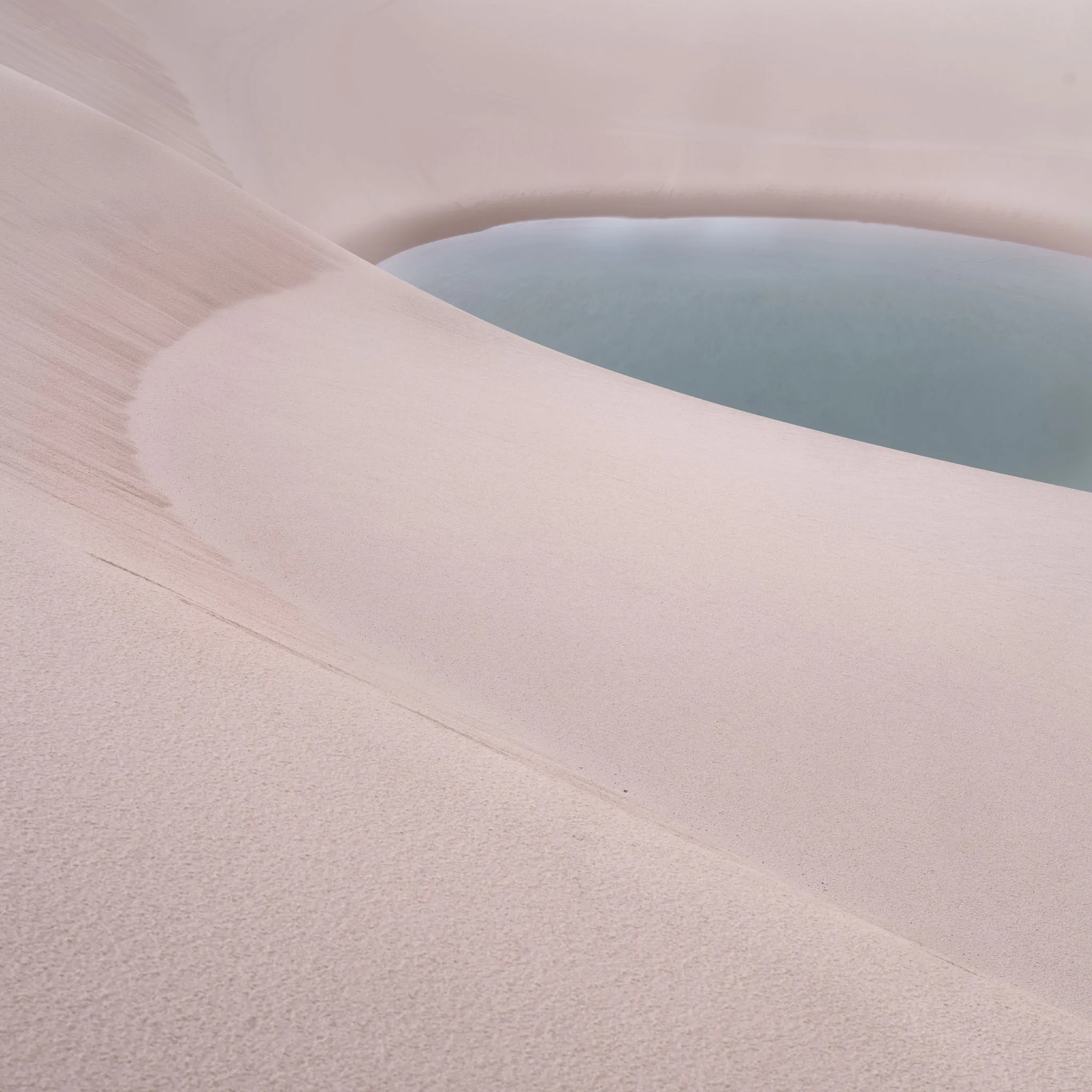 A rounded white dune ridge sweeping above a pale blue-grey lagoon