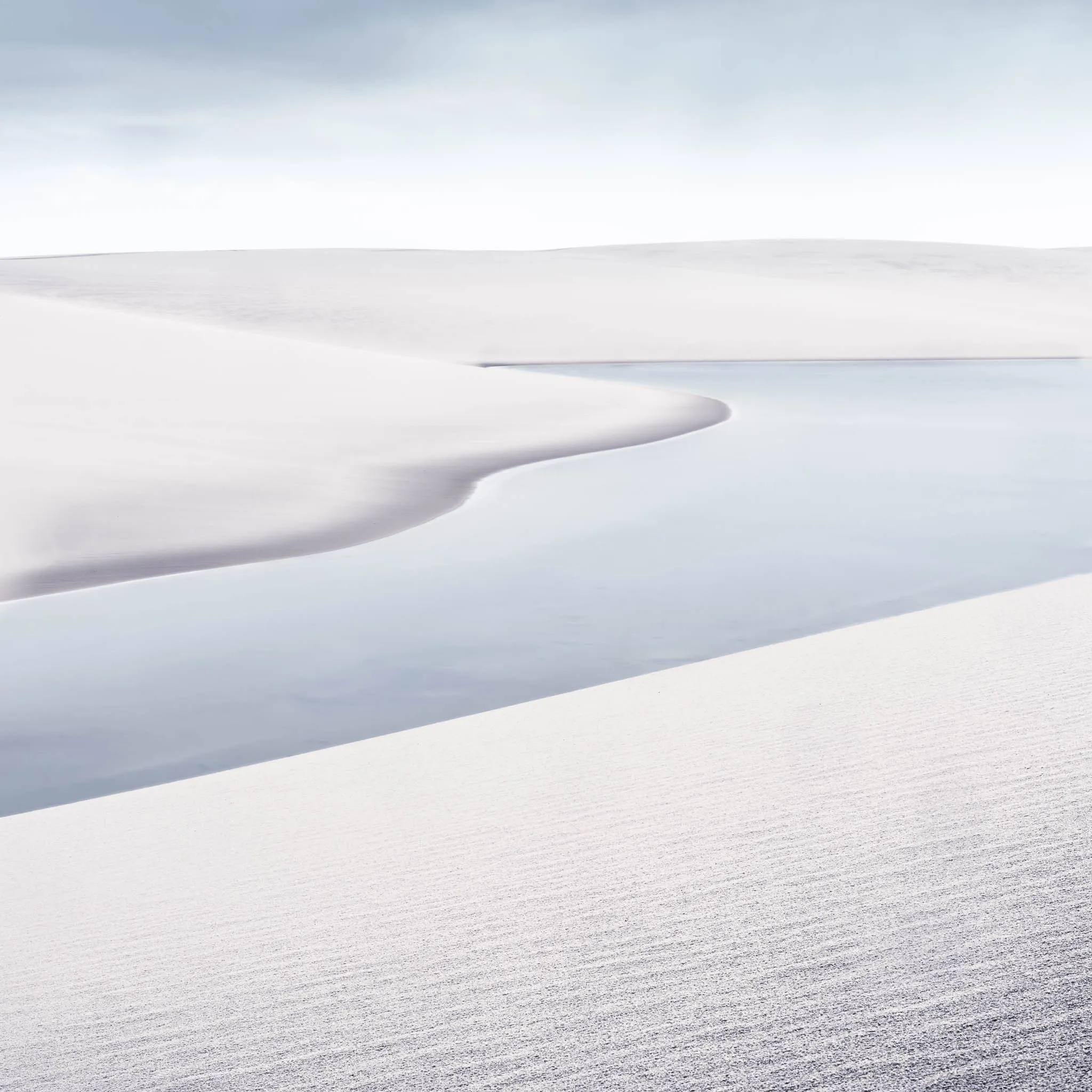 A broad white dune sweeping down to a calm reflective lagoon beneath a pale sky