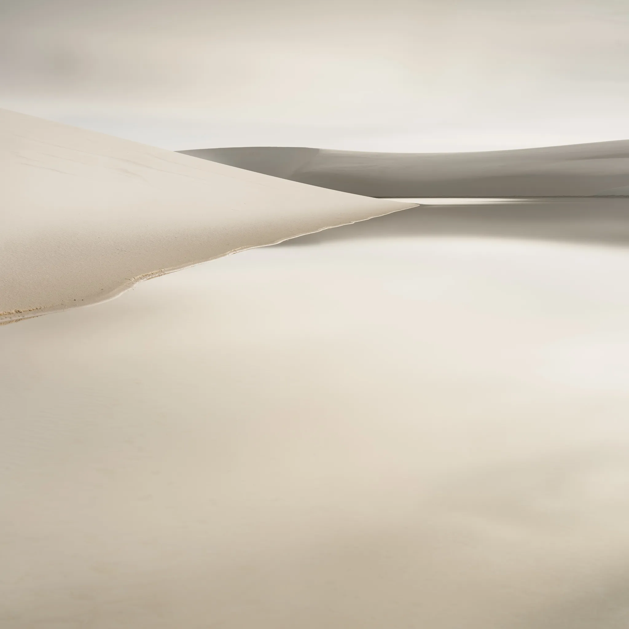 Minimal beige dune ridges meeting in a soft peak against an empty sky