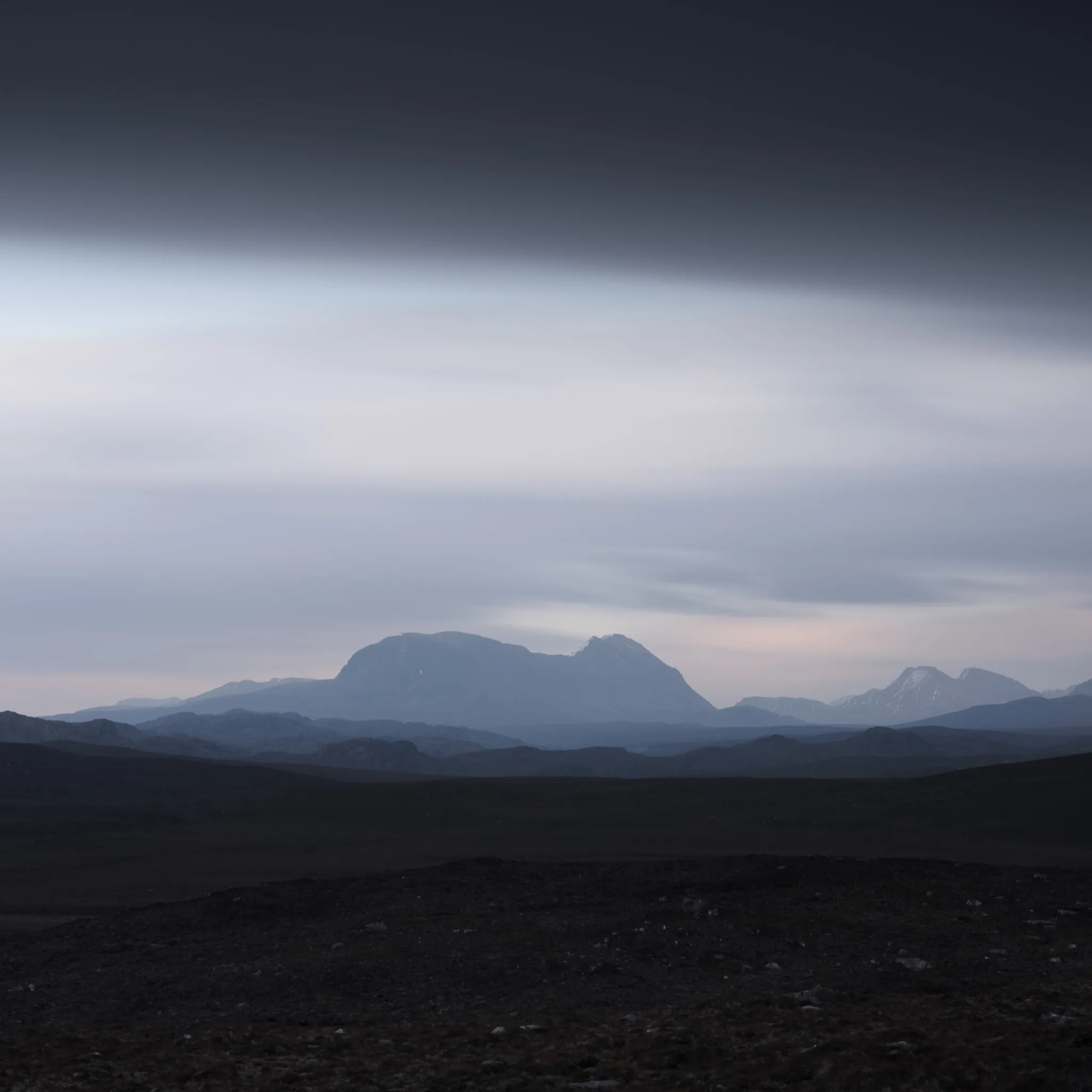Distant blue mountains rising from dark moorland under a heavy band of grey cloud