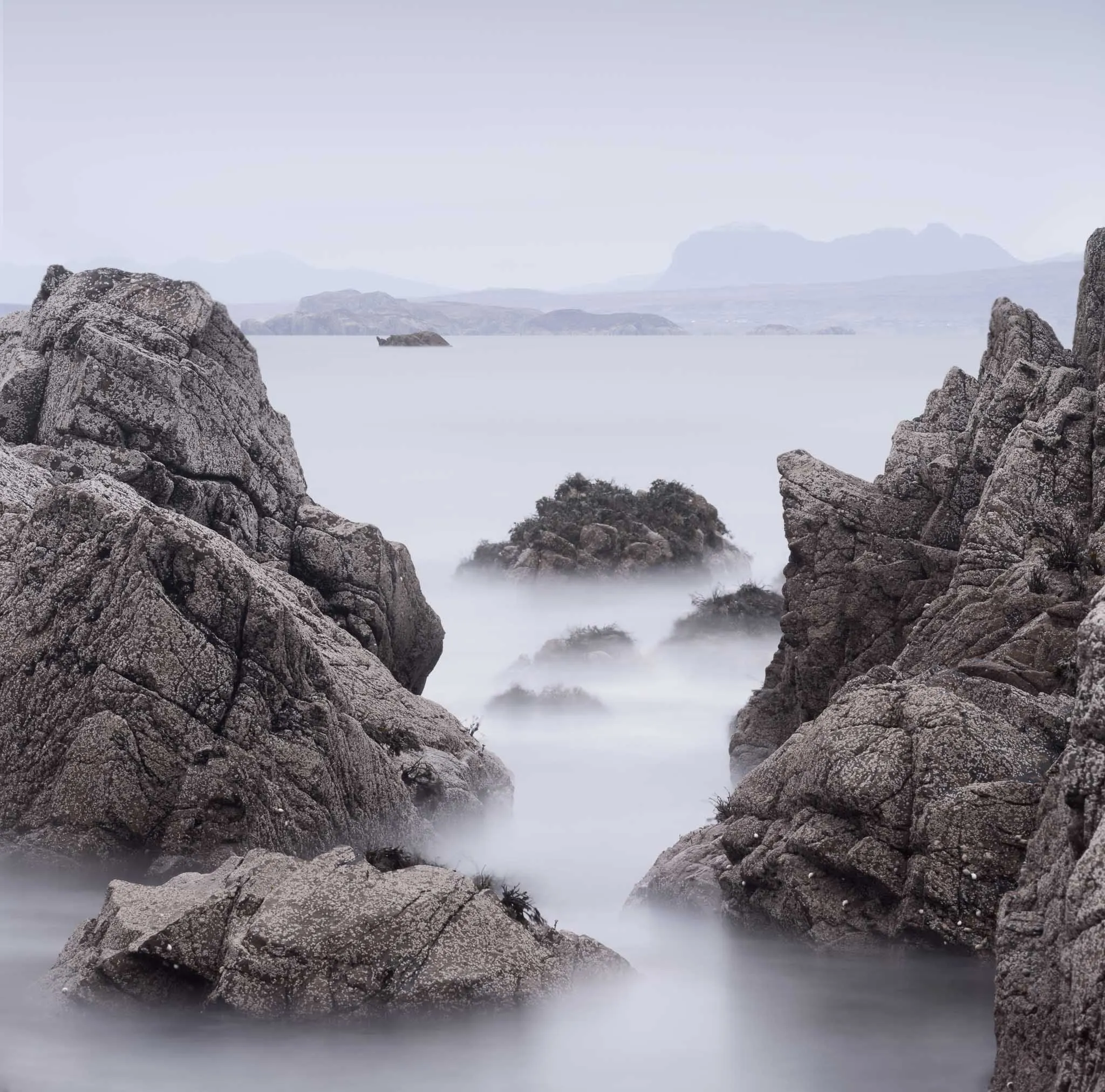 Pale, cracked granite rocks framing a silky sea with hazy headlands beyond