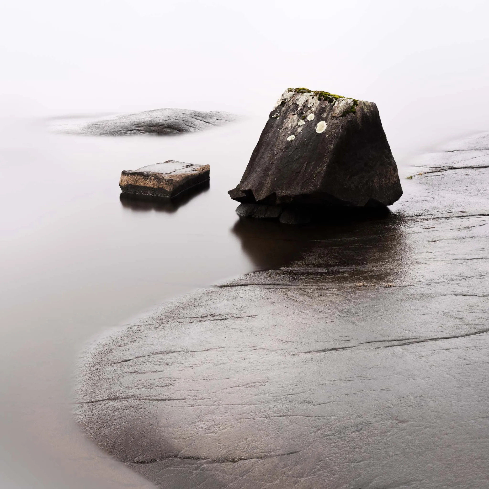 Two dark boulders on a smooth wet rock slab meeting misty, long-exposure water