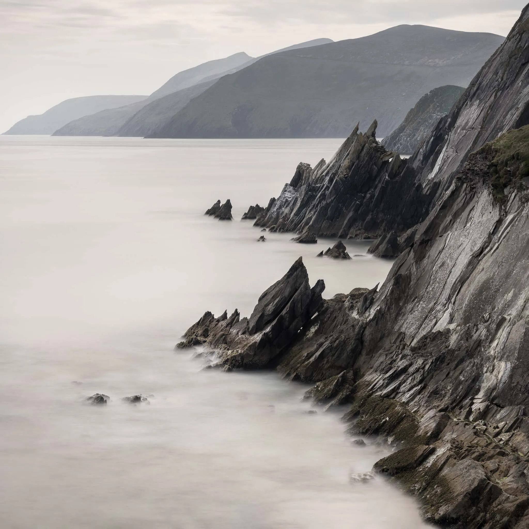 Jagged dark sea cliffs plunging into a misty sea, layered headlands fading into haze