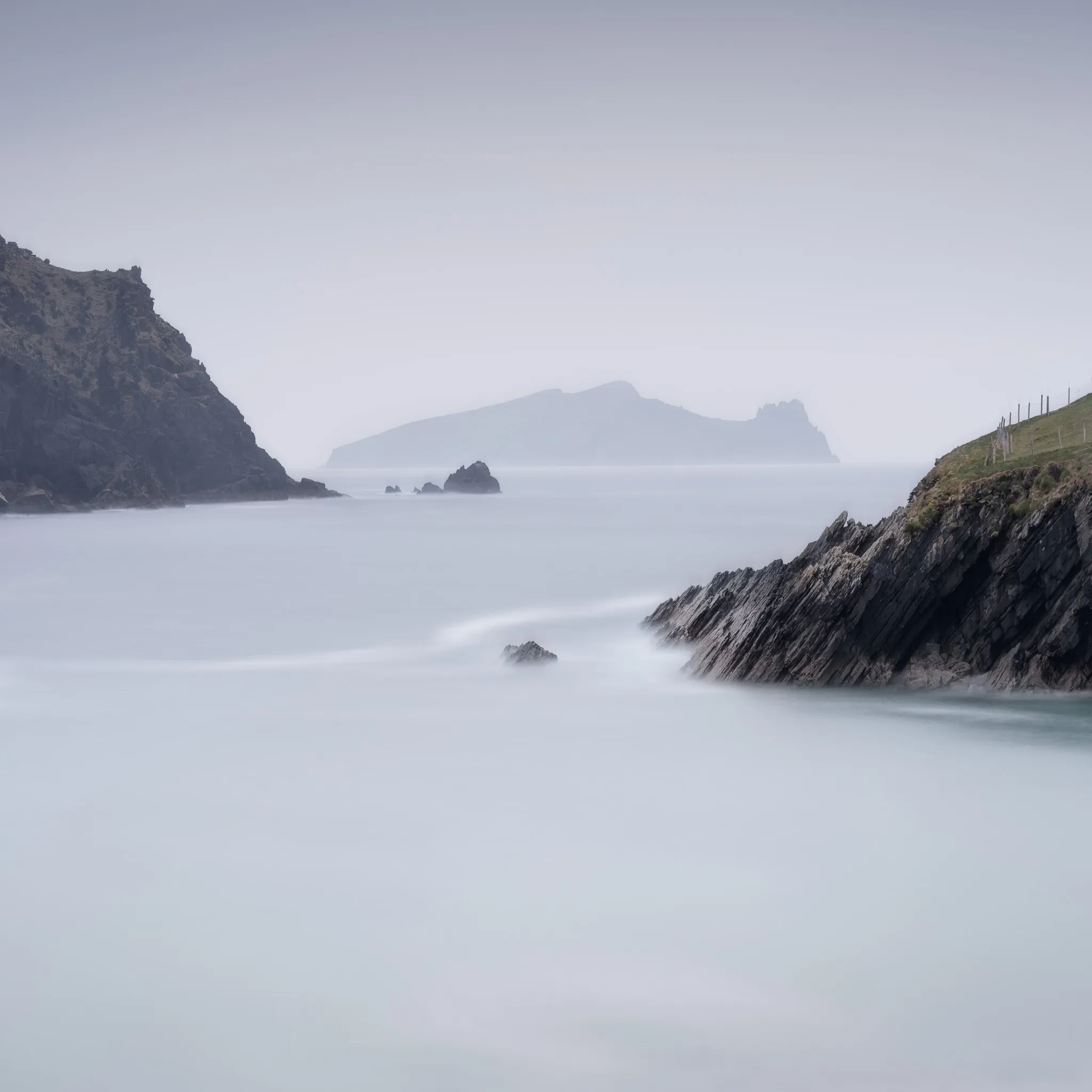 Slate cliffs and sea stacks in soft mist, a silky sea and a fog-veiled headland beyond