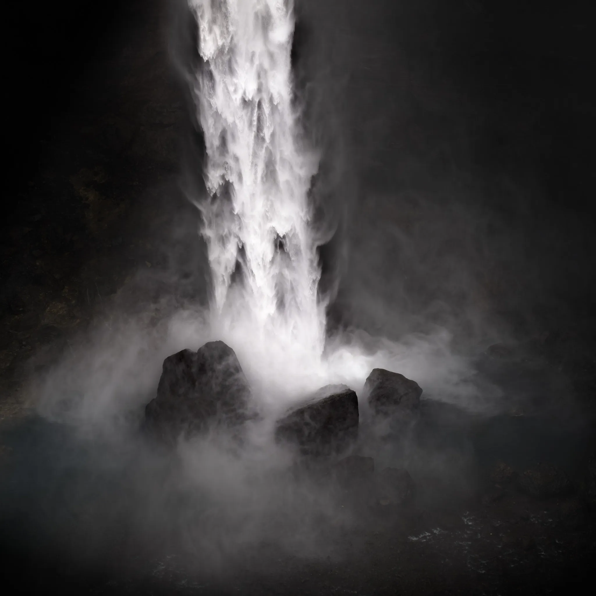 A powerful waterfall plunging onto dark rocks amid swirling spray in near-black surroundings