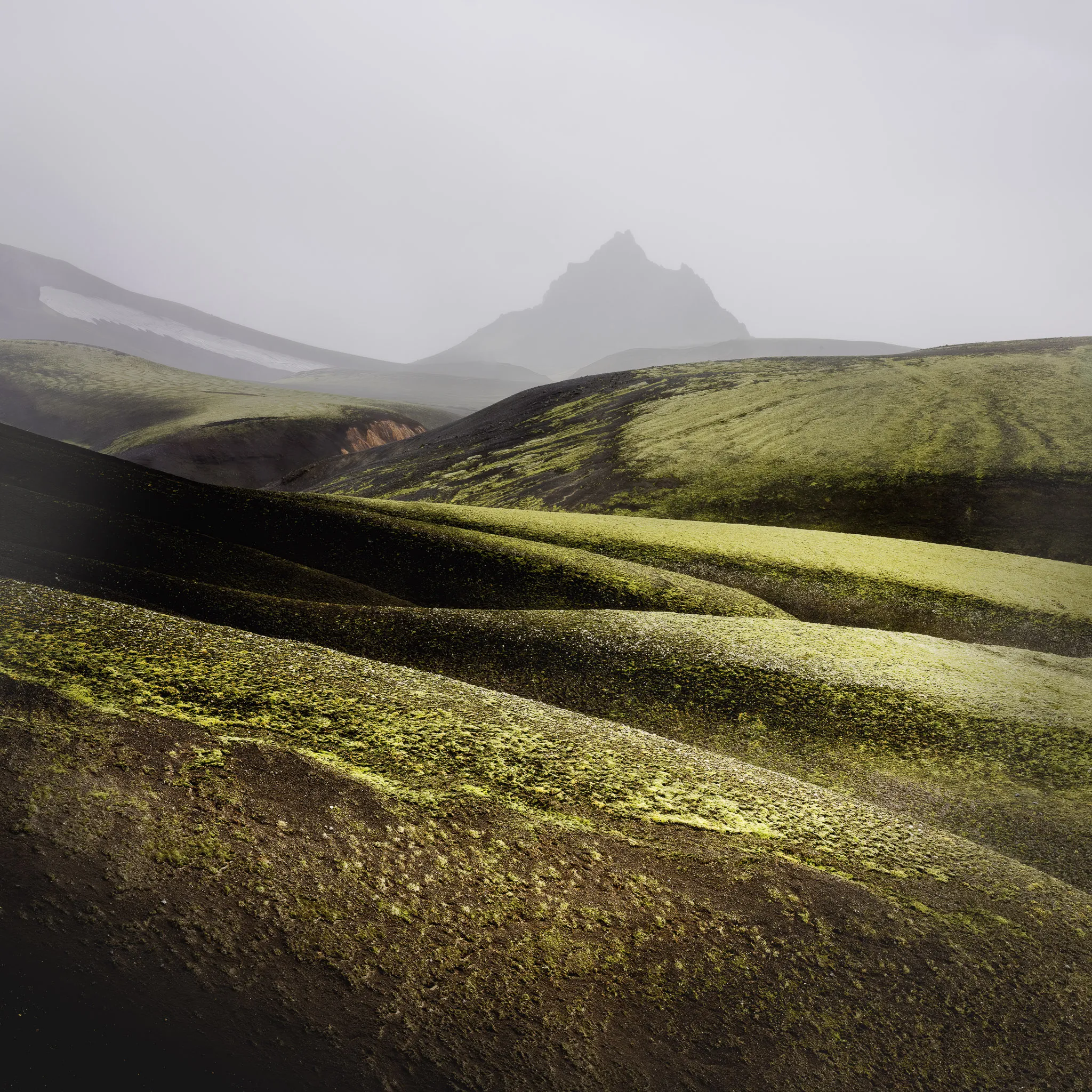 Rolling moss-green volcanic hills with a peak dissolving into mist