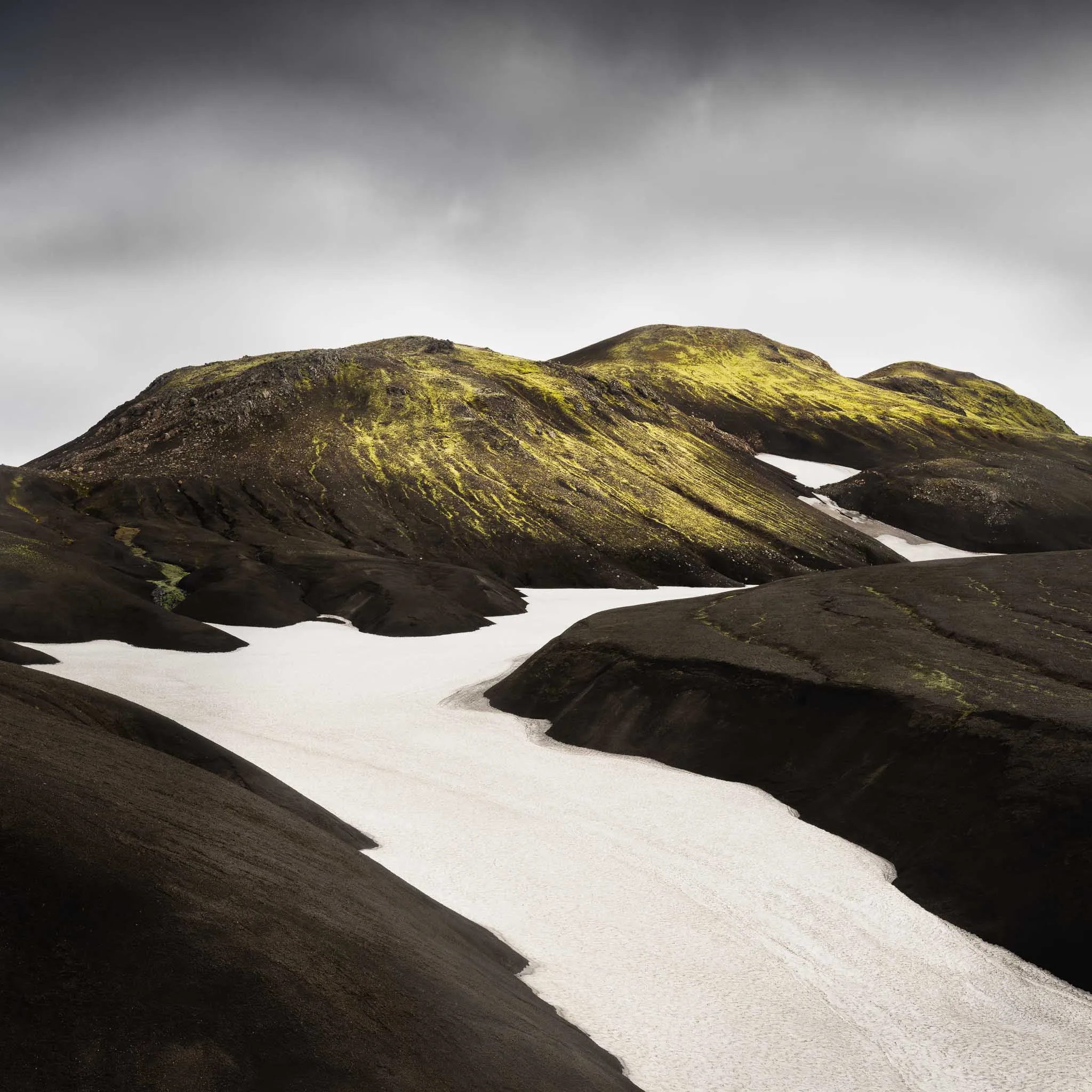 Moss-streaked black hills with a winding snowfield running through the valley