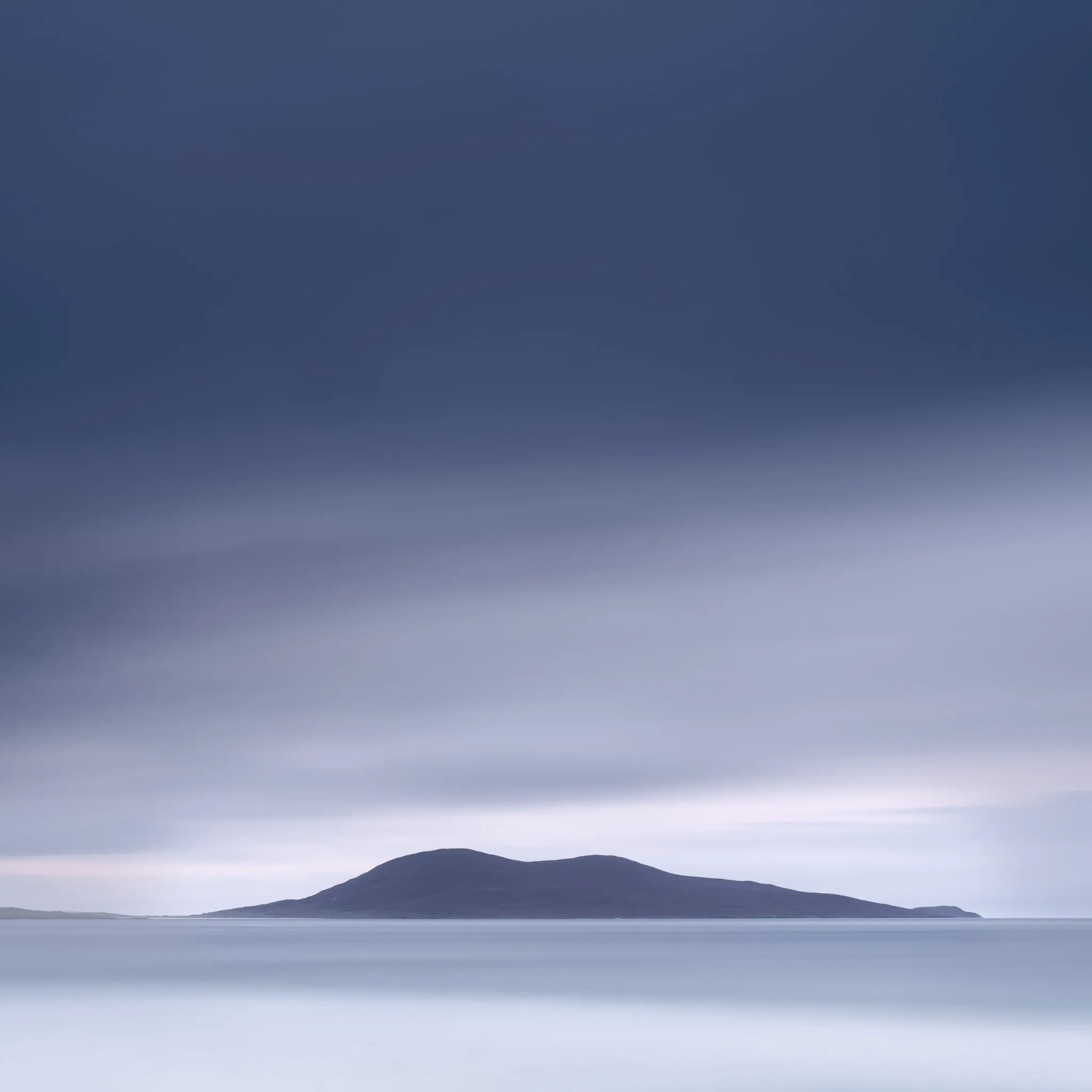 A low island silhouetted on a calm sea beneath a vast blue-grey sky