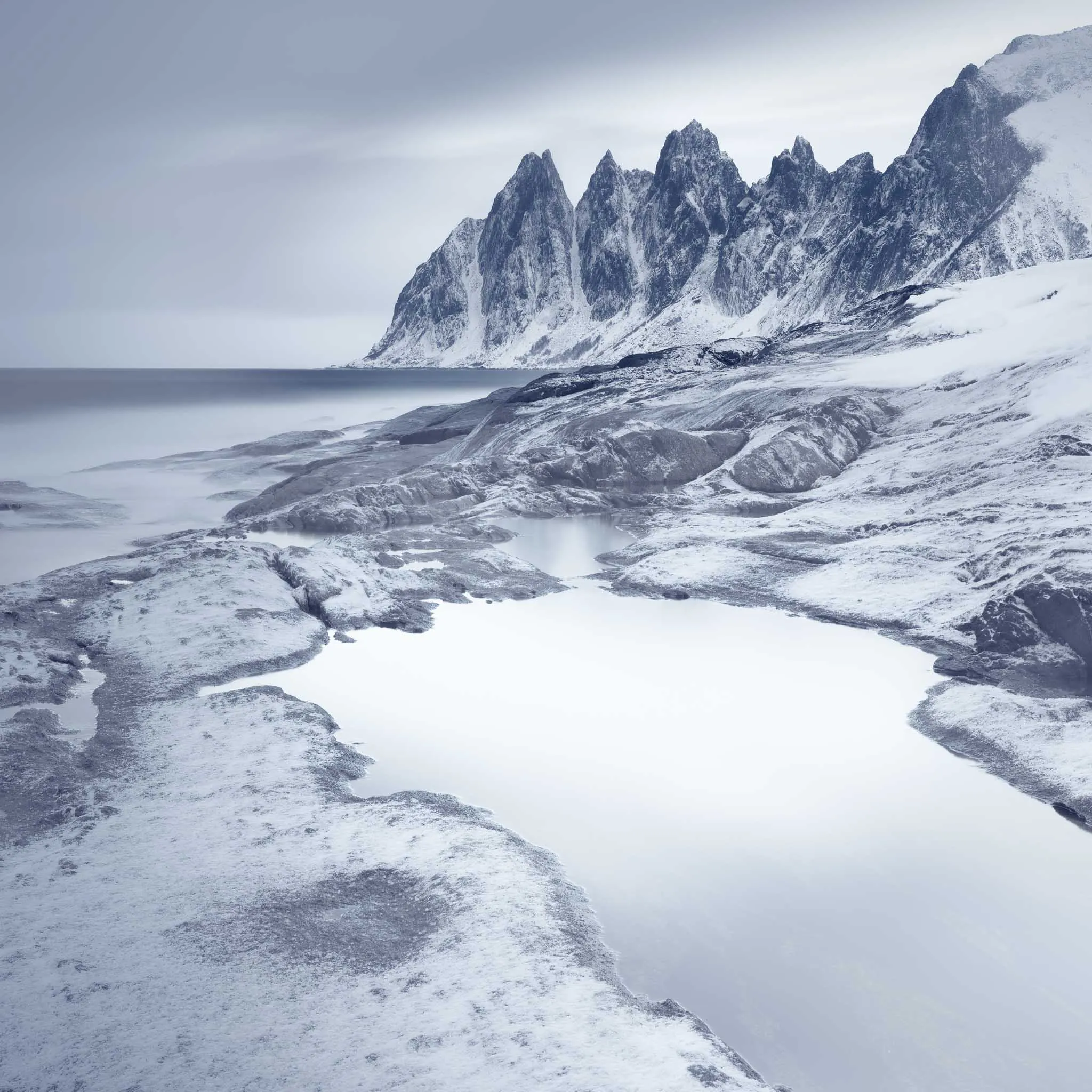 The toothed ridge of Okshornan reflected in a still tidal pool among snow-dusted rocks
