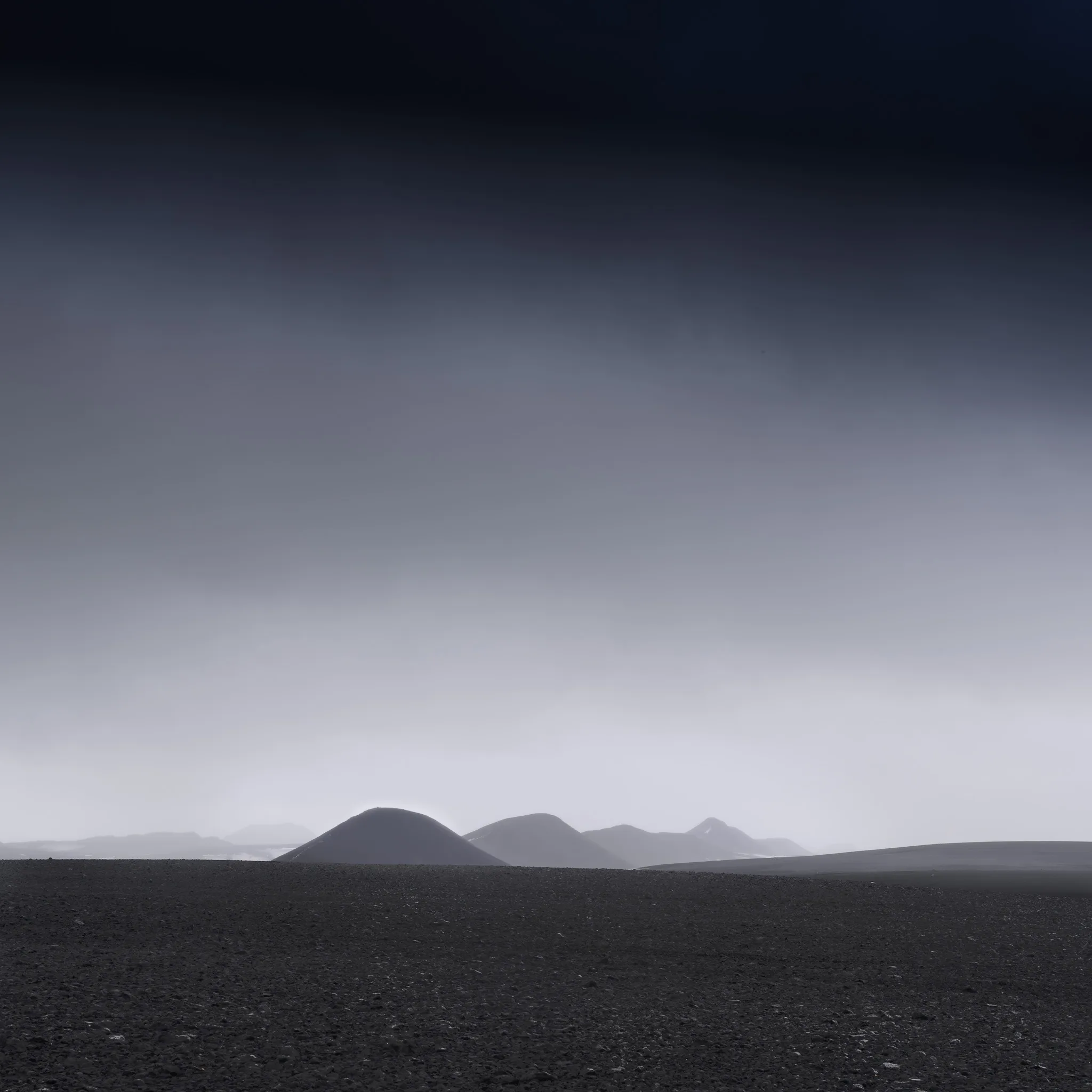A dark volcanic cone rising from a black desert plain under a soft grey sky