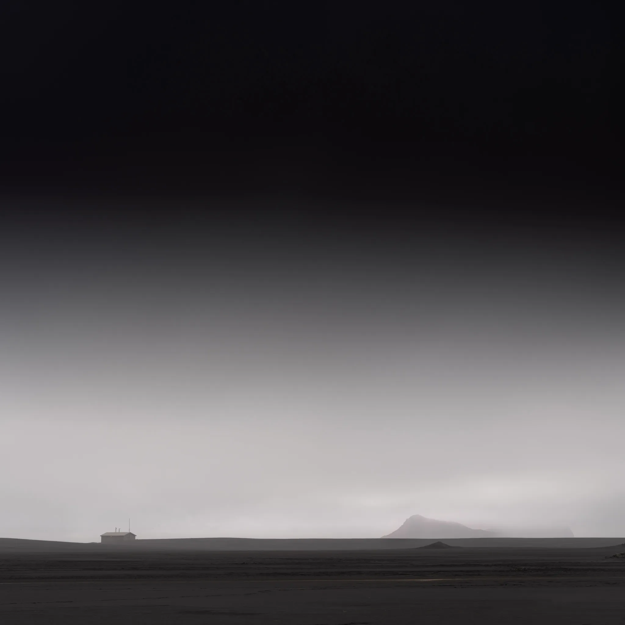 A lone small hut on a vast black volcanic plain with a faint mountain lost in mist