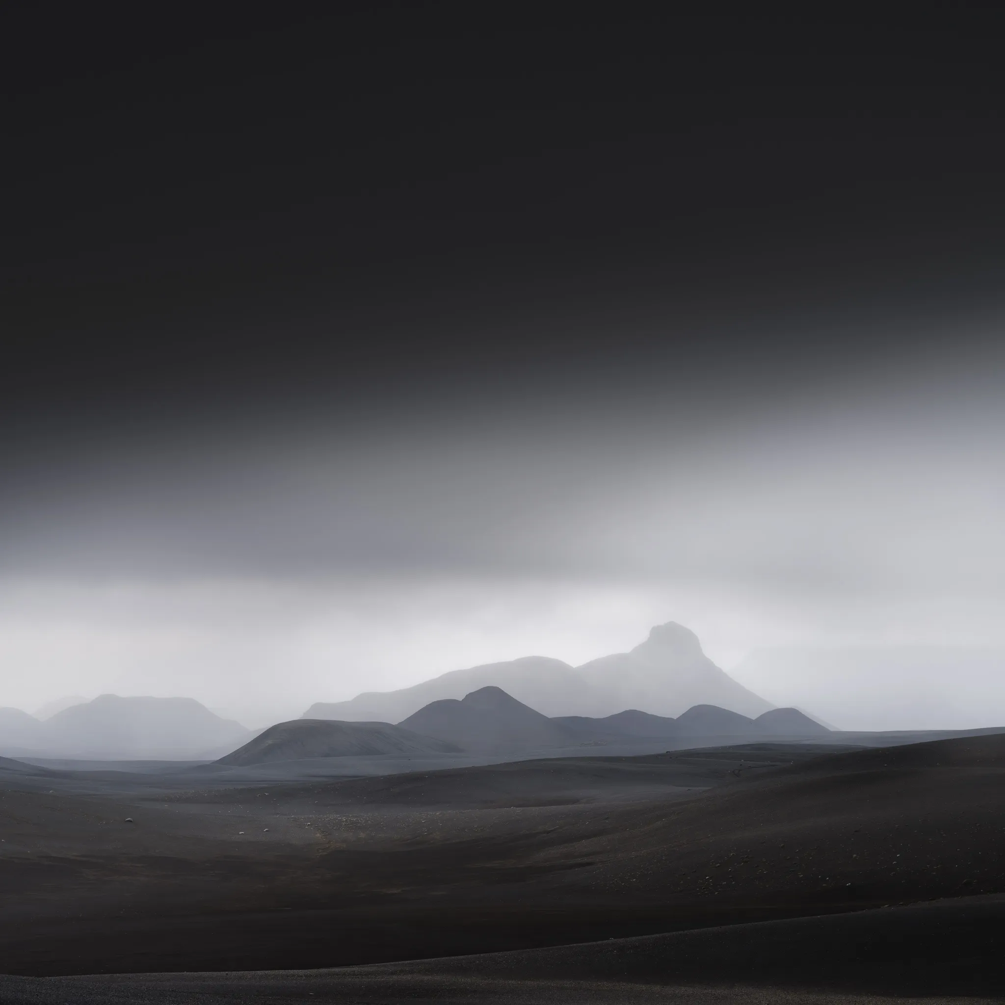 Misty dark hills and a peak rising over a black volcanic plain beneath low cloud