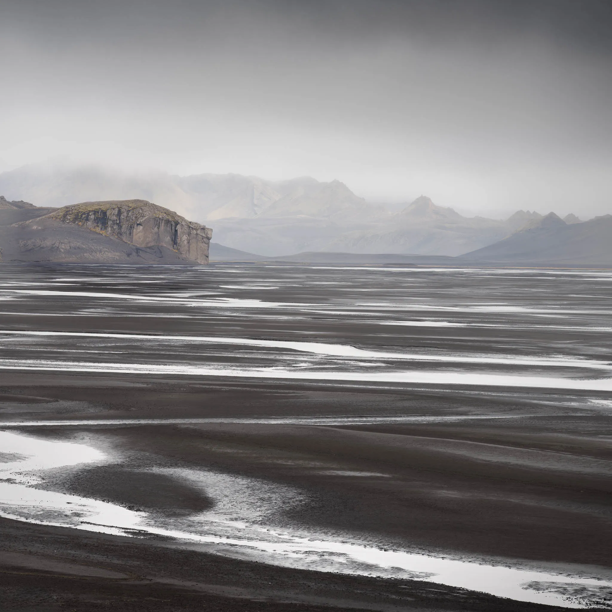 A braided black river delta laced with silver channels, a flat-topped crag and misty mountains