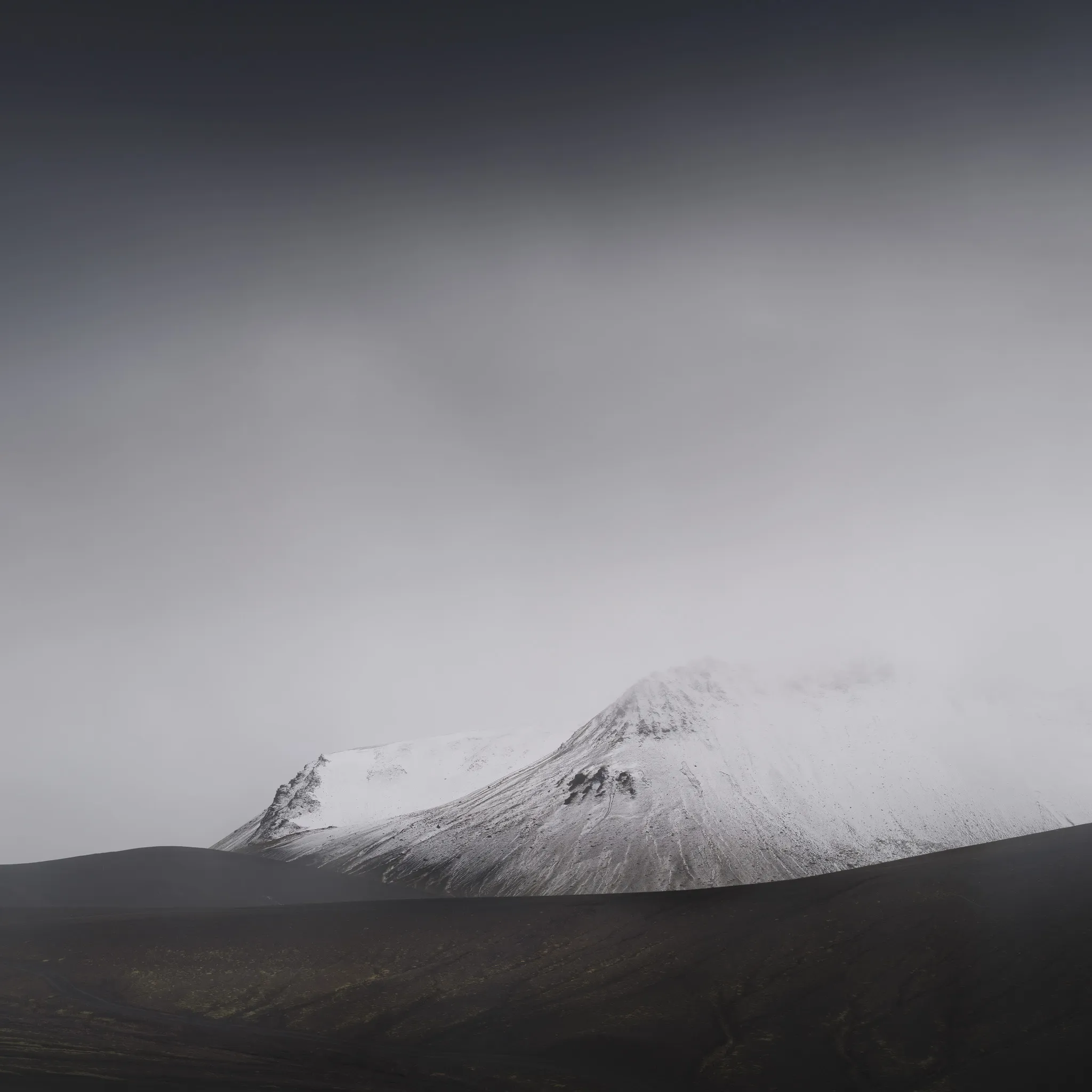 A snow-covered mountain flank emerging from mist above a dark volcanic slope