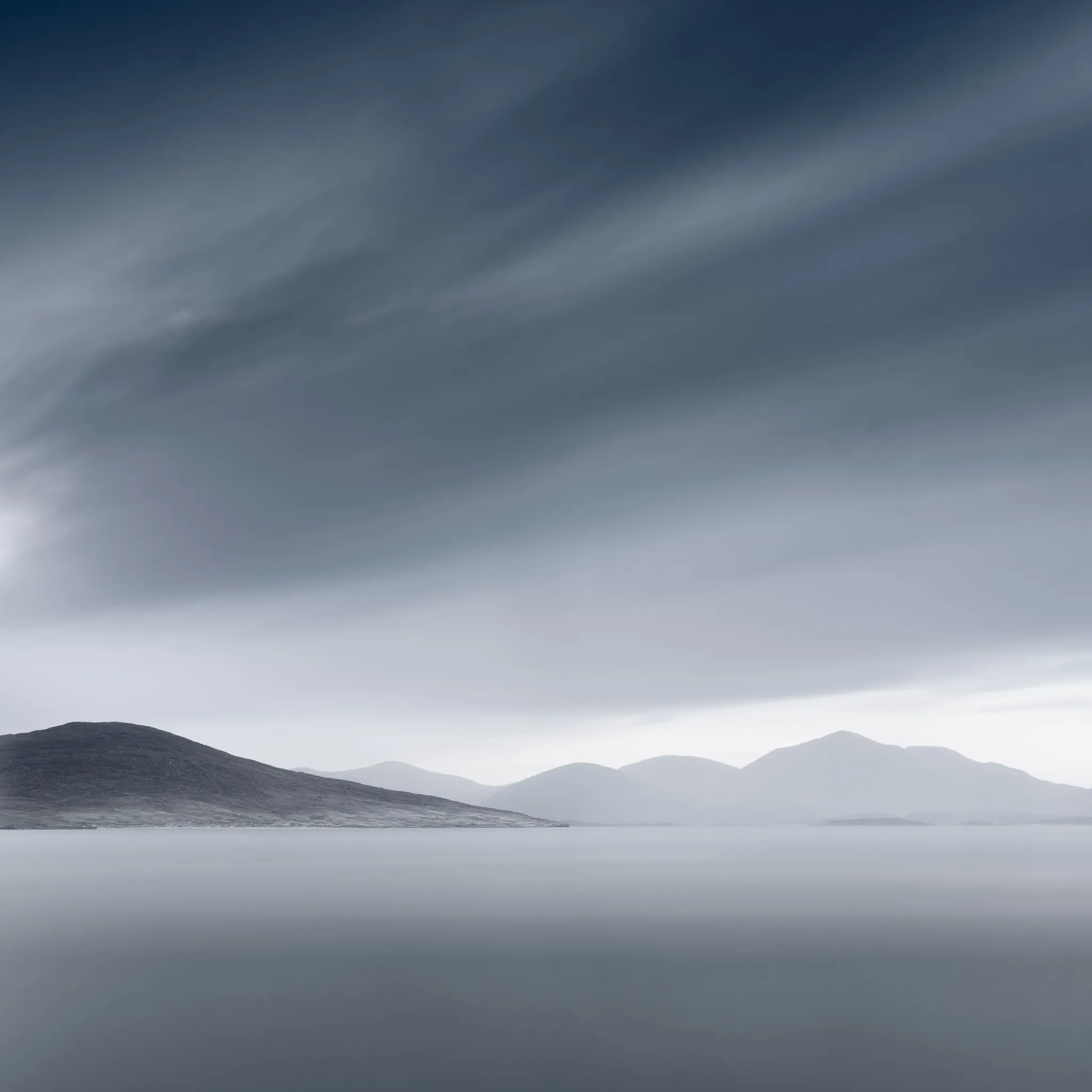 Layered hills fading into mist across calm water under a dramatic sky