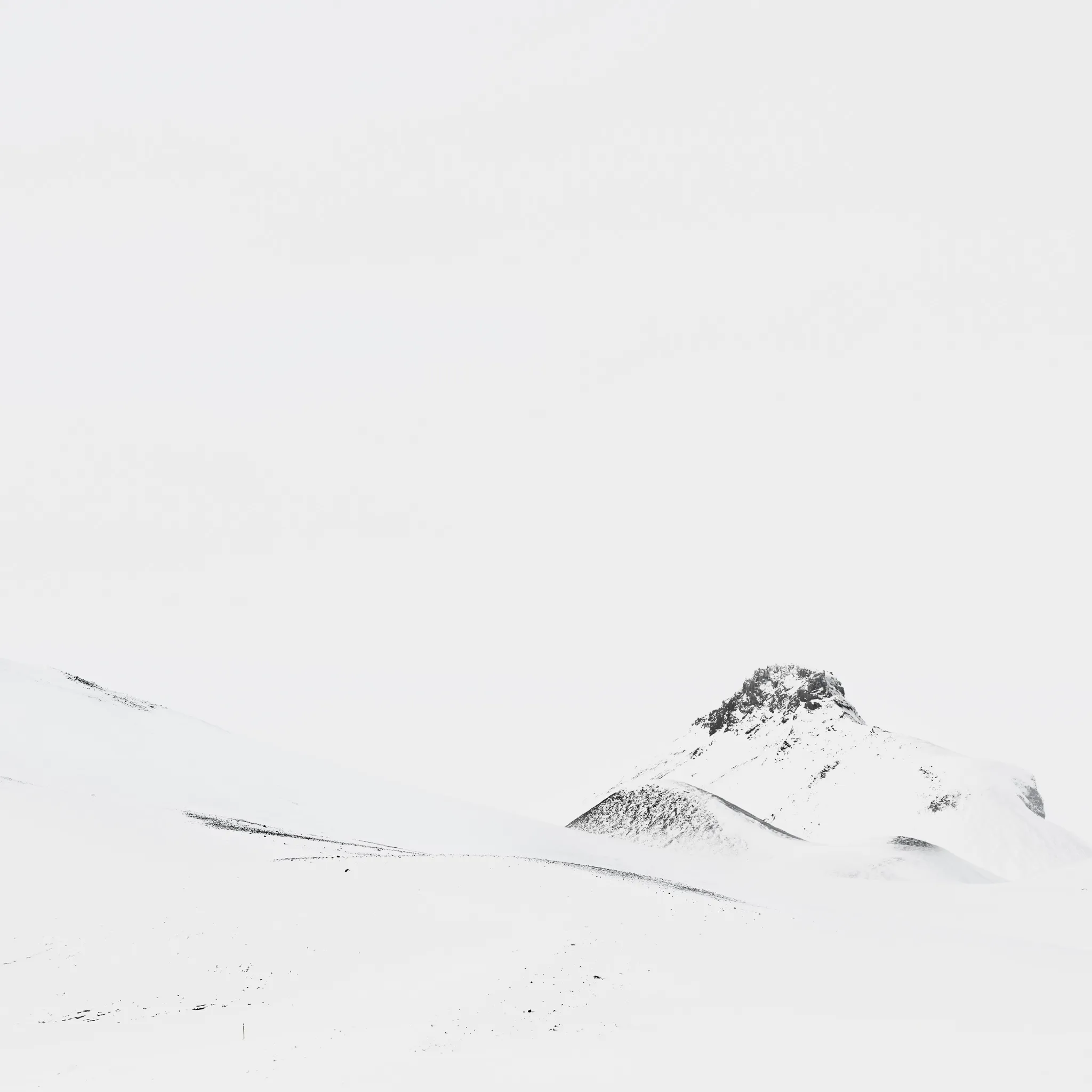 A single dark rocky peak emerging from an almost pure-white expanse of wind-smoothed snow