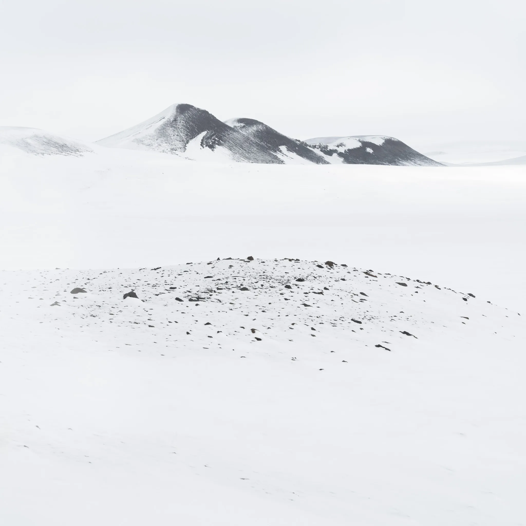 Dark twin peaks above a low mound of snow-flecked black rubble on a white plain