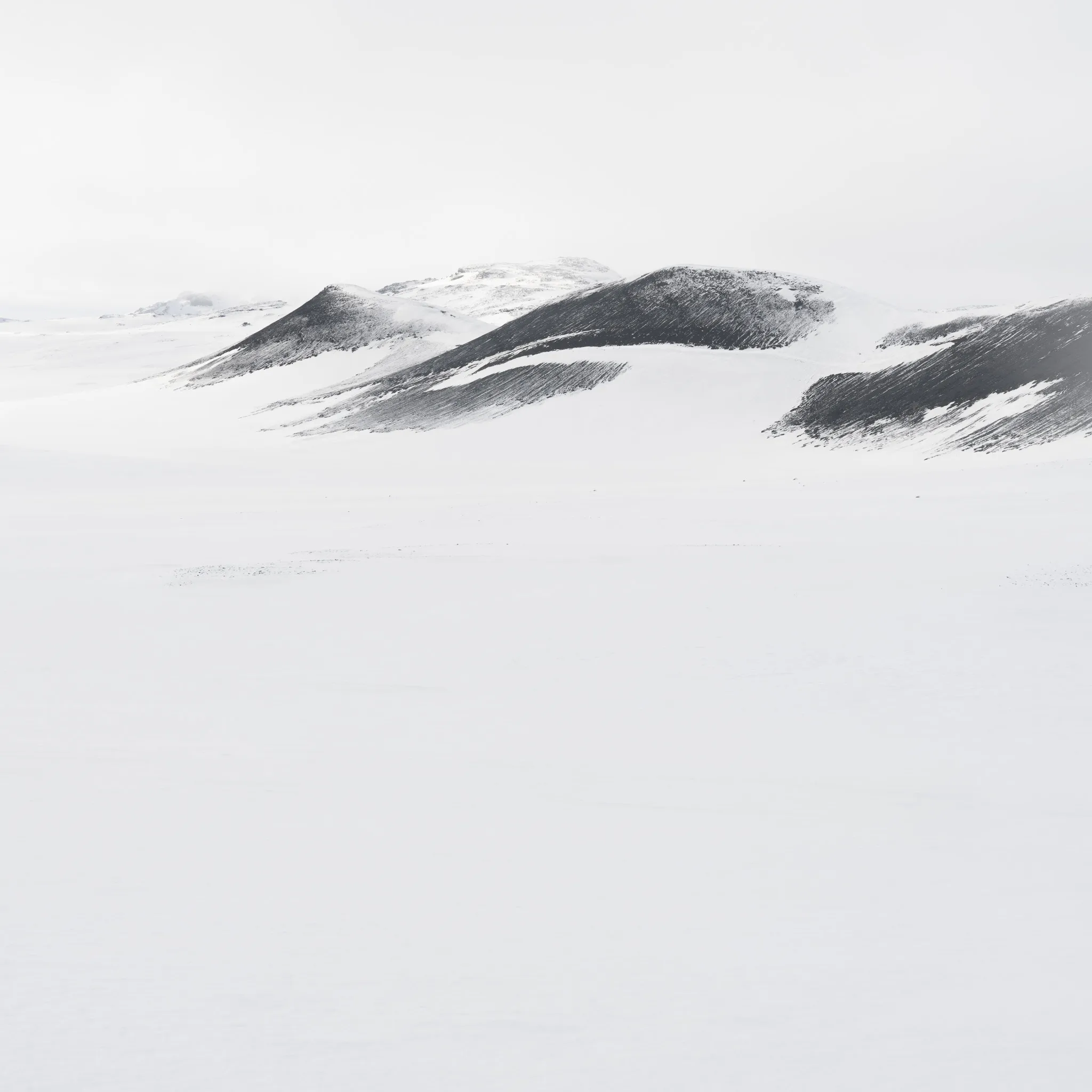 A receding line of hills streaked with dark, brushstroke-like exposed rock under a pale sky