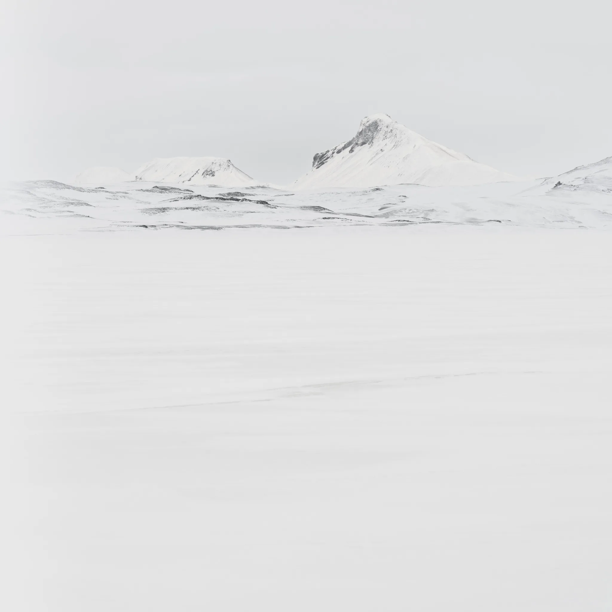 Snow-clad peaks barely separated from a white sky above a vast, empty snowfield