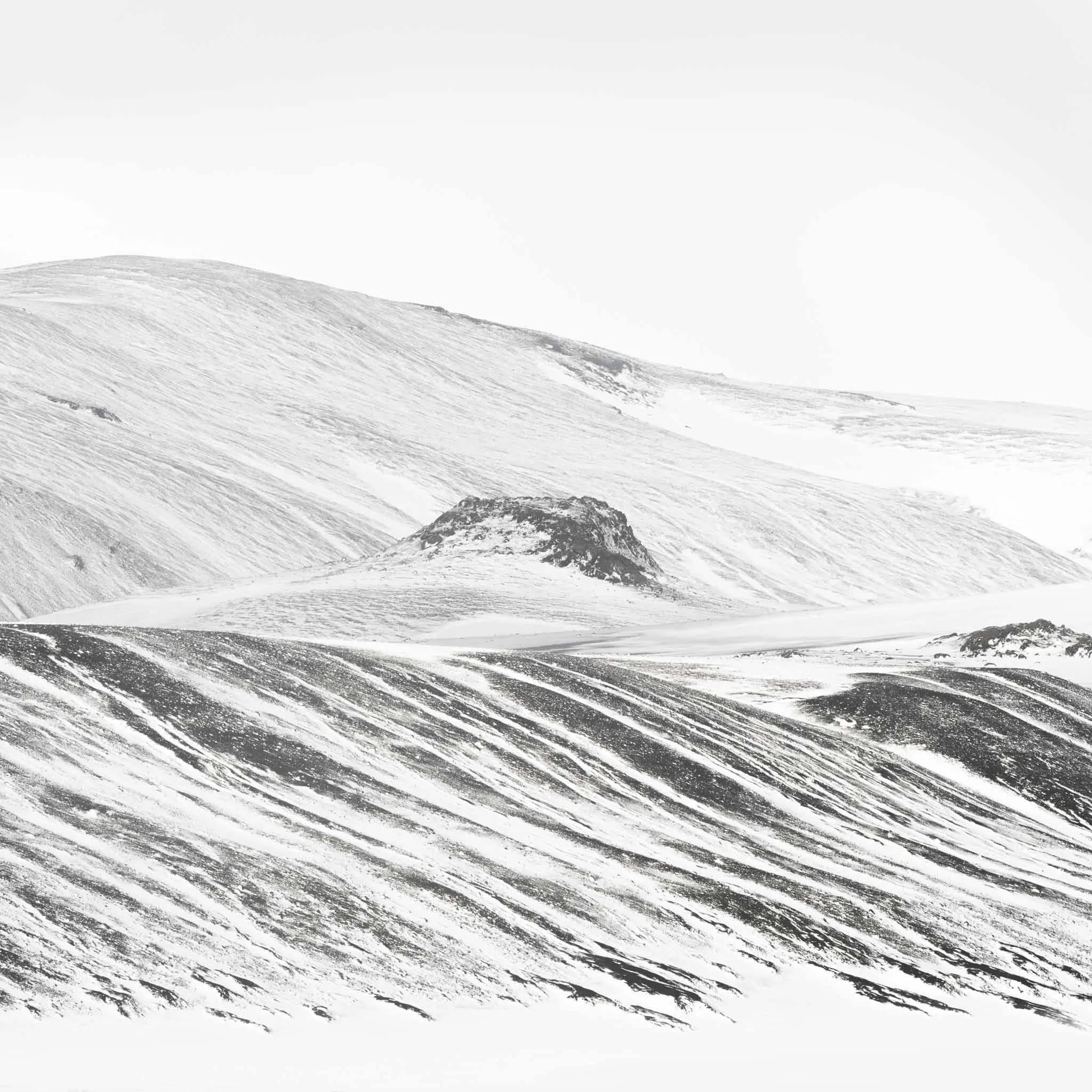 Diagonal ribbons of black lava showing through wind-blown snow, like ink brushstrokes across a white canvas