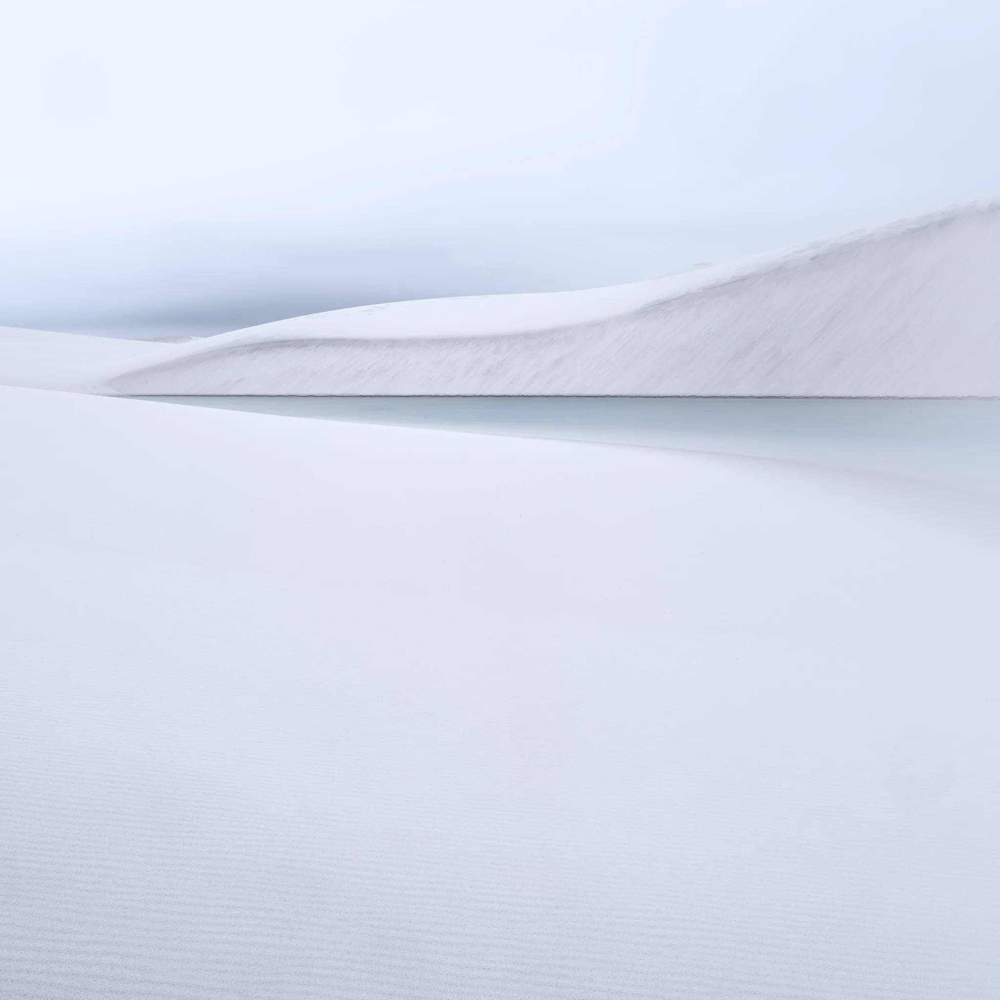 A white dune ridge above a still lagoon, finely rippled sand in the foreground