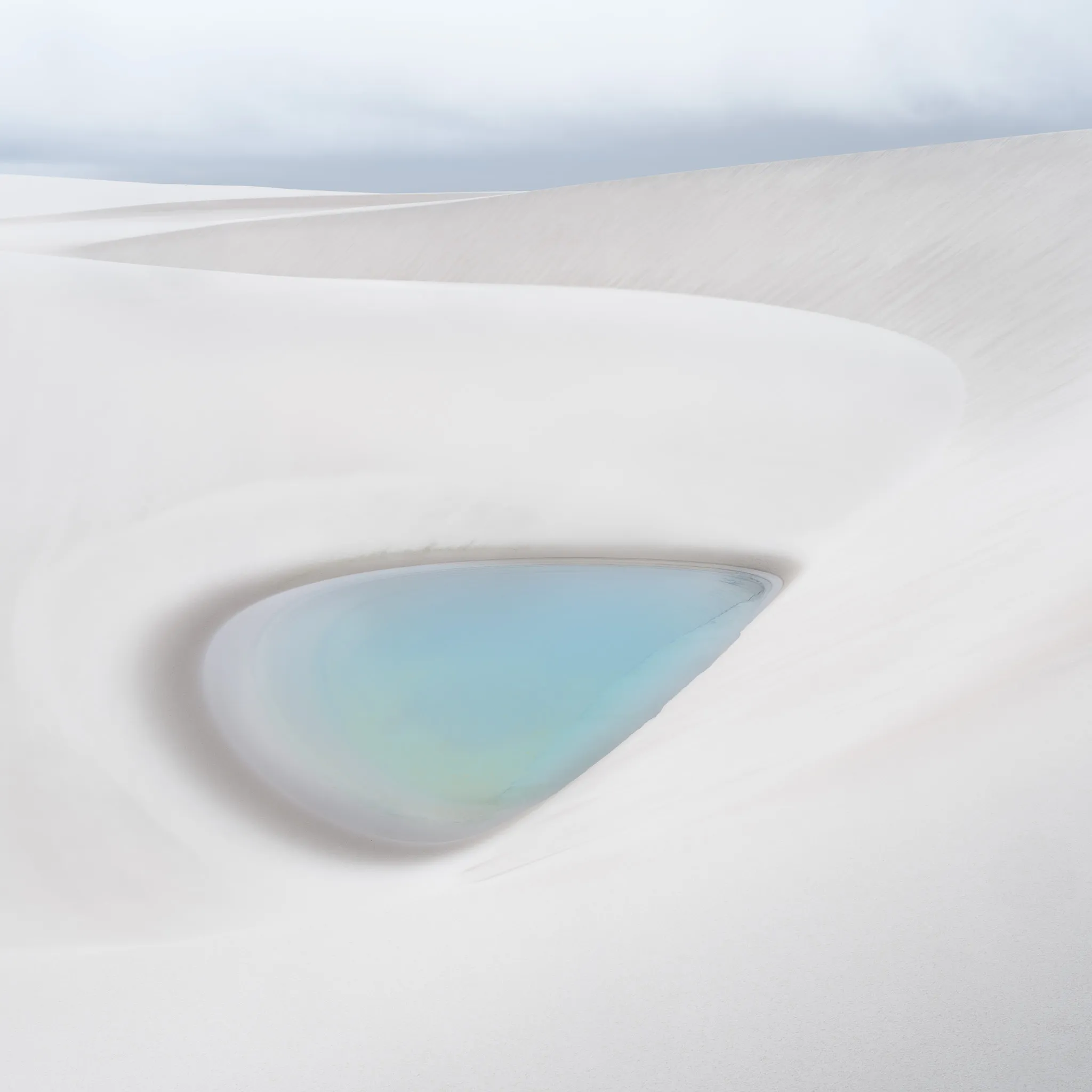 A teardrop-shaped turquoise lagoon nestled in a smooth white bowl of sand
