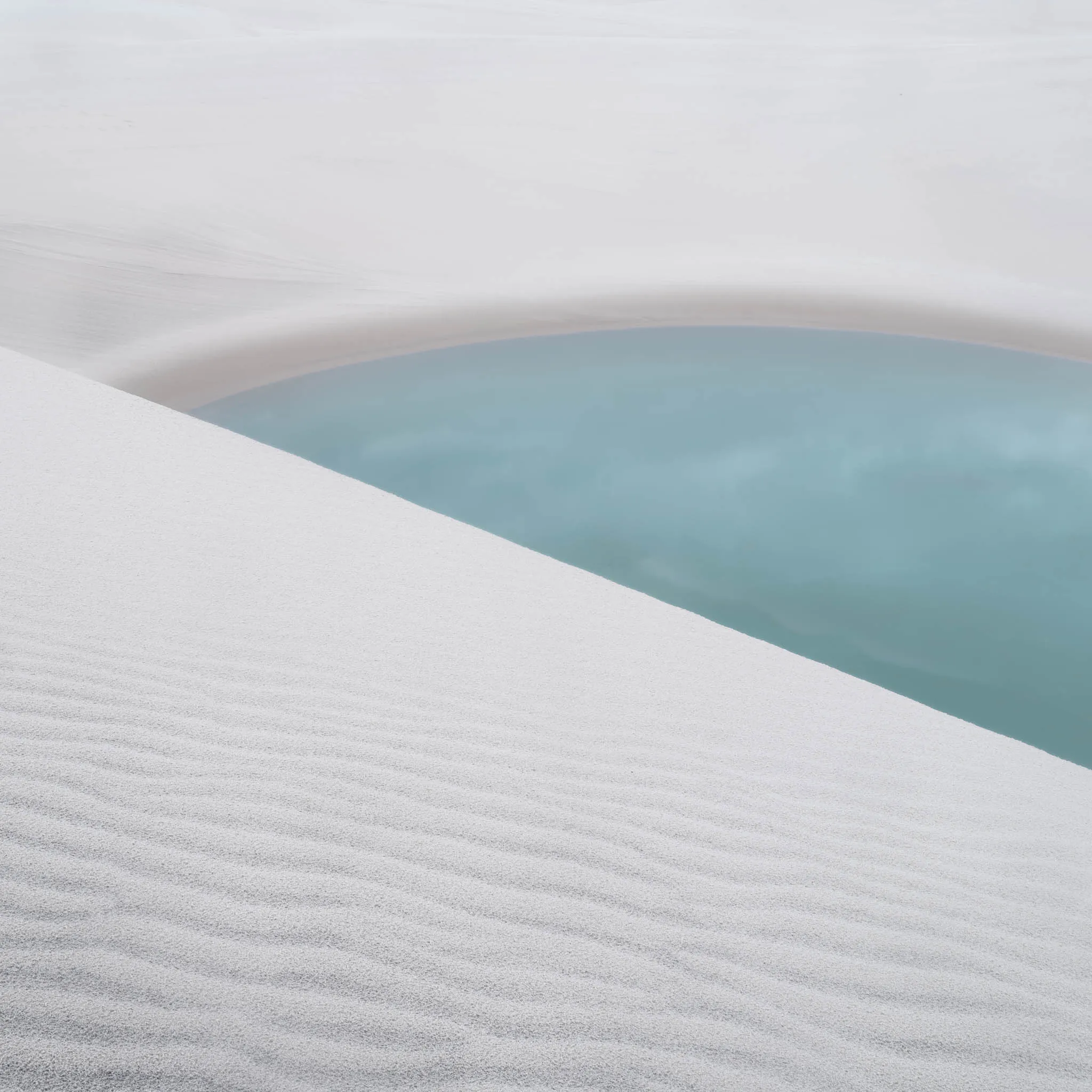 A diagonal ridge of rippled white sand beside a still turquoise pool