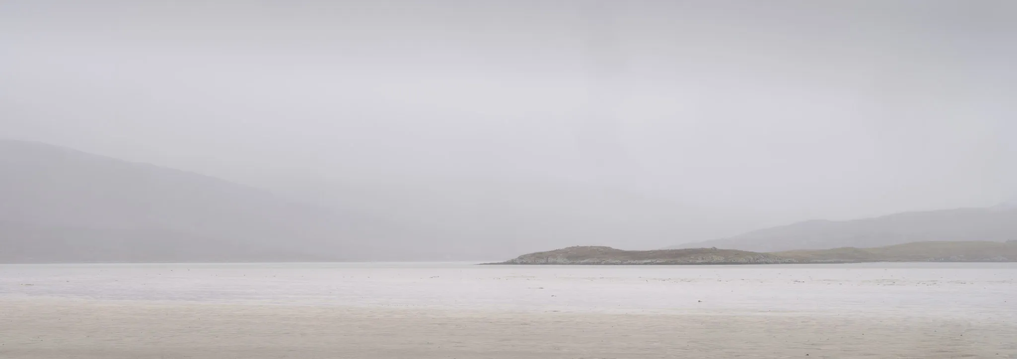 A low rocky island in a misty estuary, soft grey and beige tones dissolving into fog