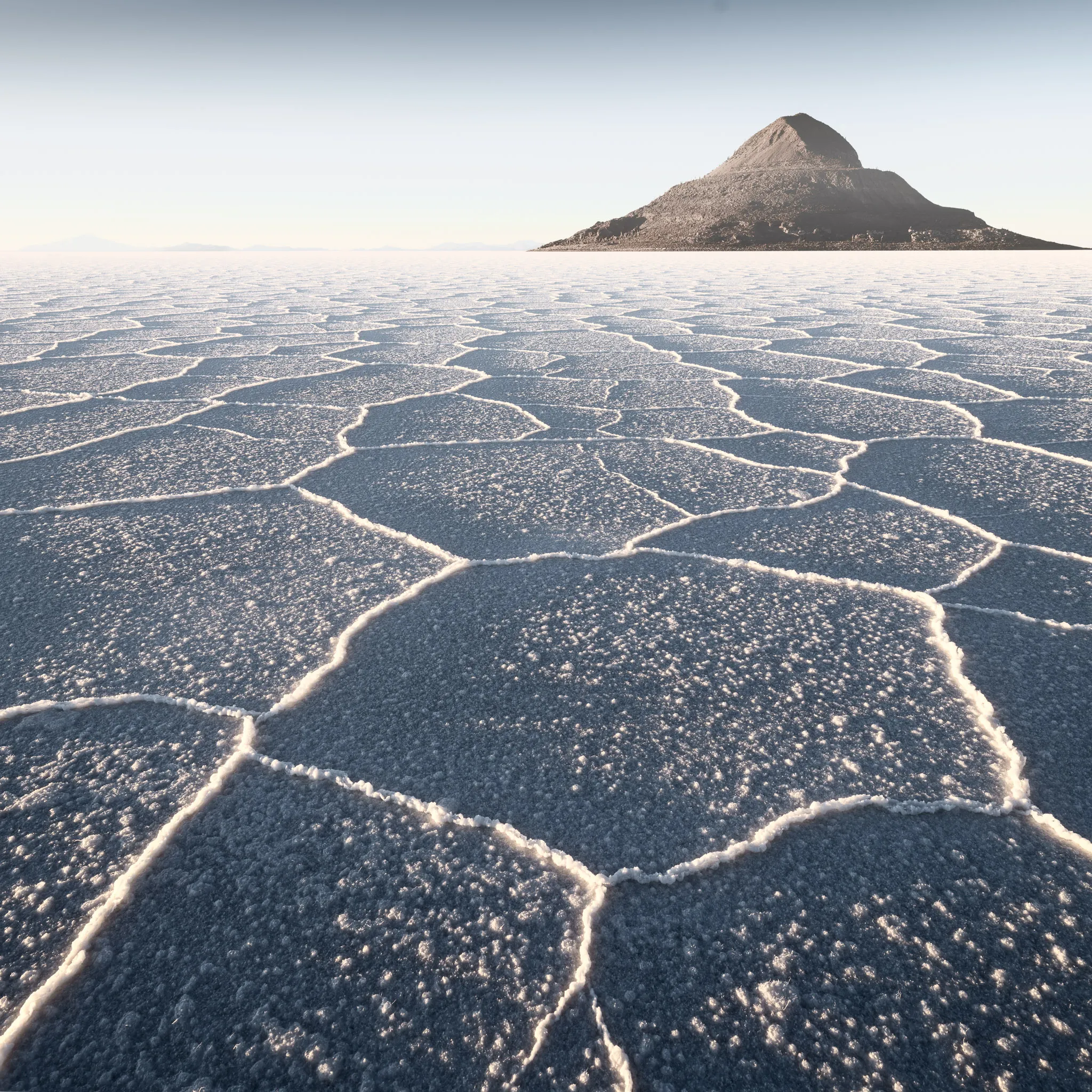 Hexagonal salt-crust patterns stretching across the salt flat toward a lone pyramid-shaped island